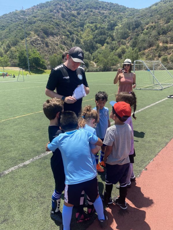 professional soccer coach teaching children how to play soccer. Coach is with a group of 4year olds in their soccer class