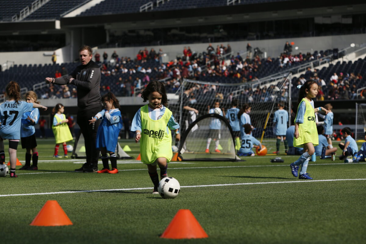 4 year old boy playing soccer. Being coached soccer bya professional soccer coach. The boys is playing with 5 year olds, 6 year olds and 7 year old boys and girls