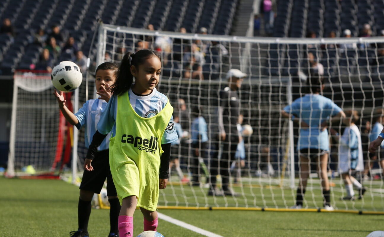 Young girl engaging in a SoCal Youth Sports soccer class, showcasing her skills as she kicks a football on the field. Experience affordable, professionally-coached soccer classes in Southern California