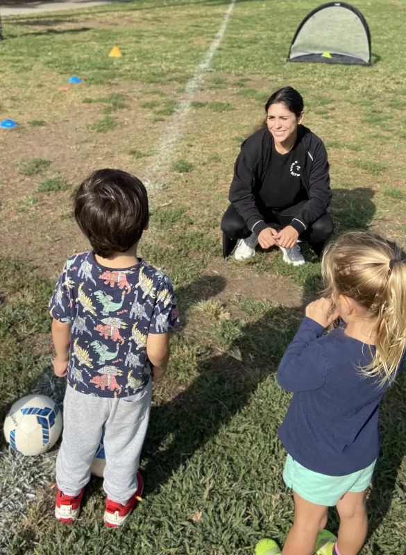 A soccer coach guiding a mom, dad, grandmother, and toddler during a parent-child class in the park